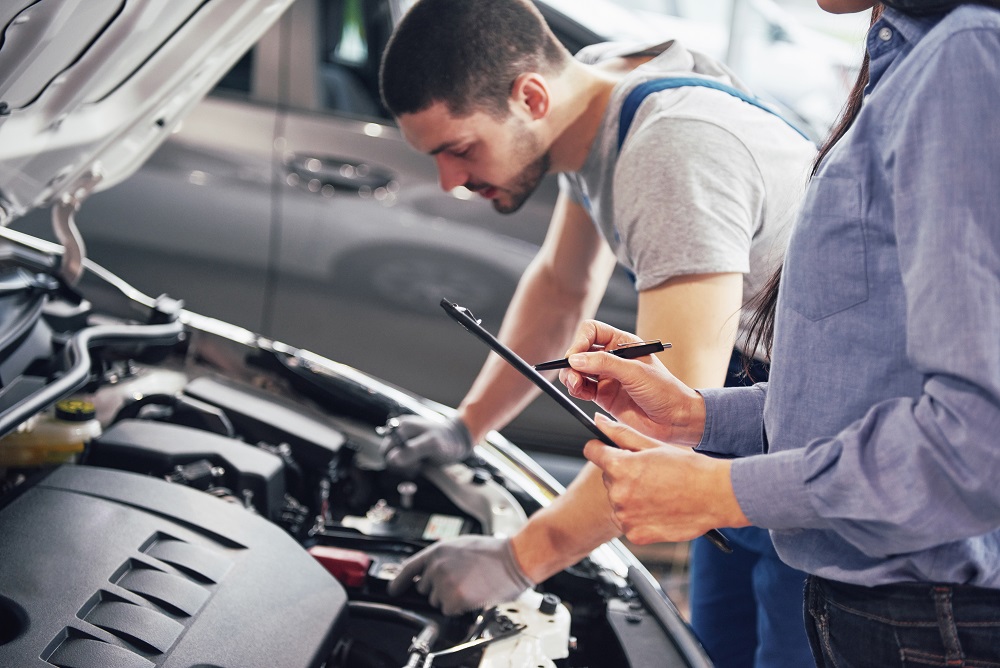 A man mechanic and woman customer look at the car hood and discuss repairs.